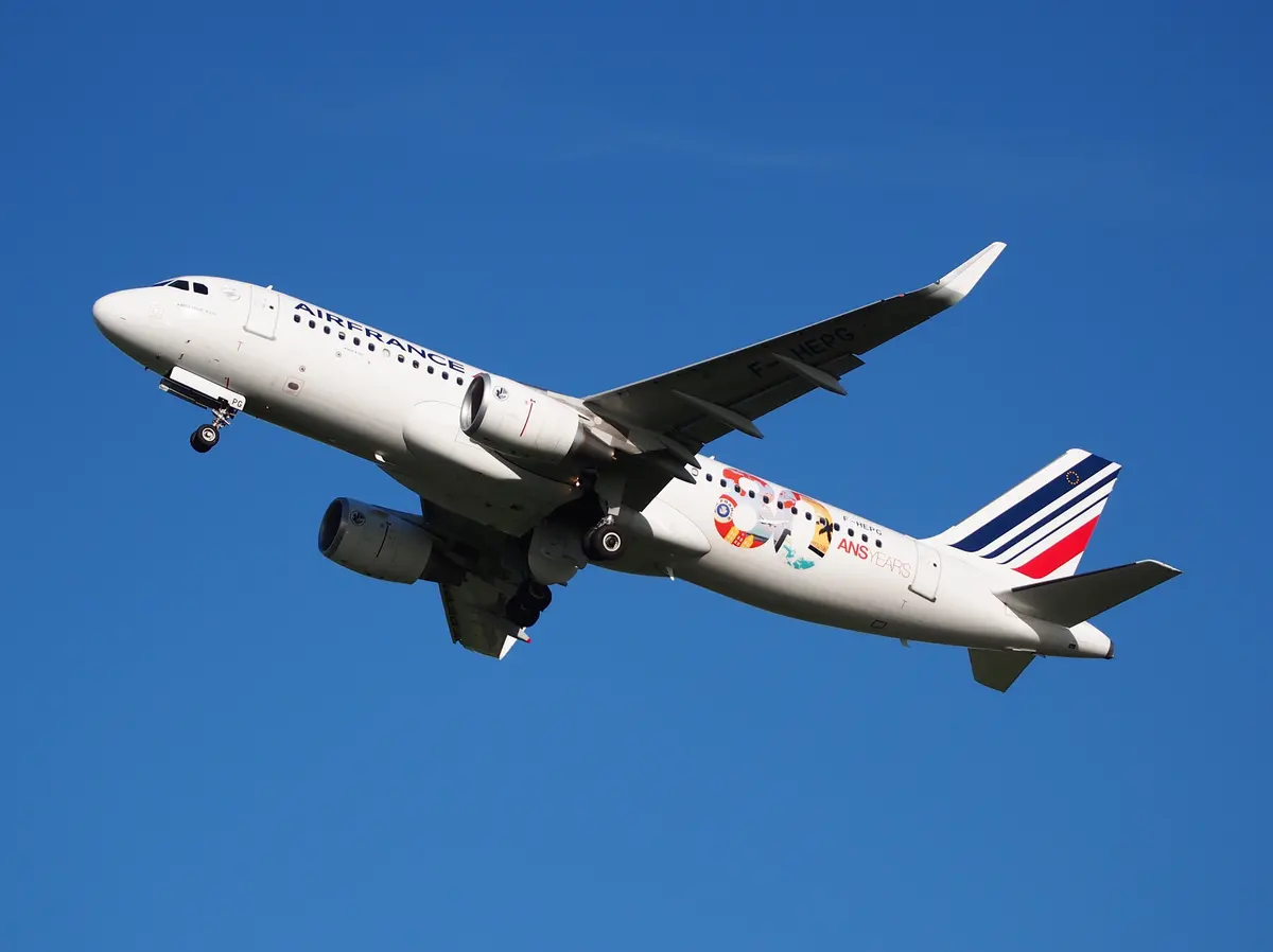 An Air France Airbus A320 in a special livery climbing out against a deep blue sky.