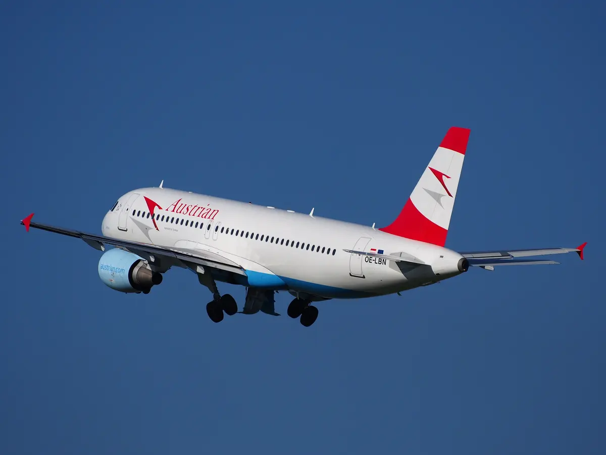 An Austrian Airlines Airbus A320 climbing after take-off against a deep blue sky, gear still down.