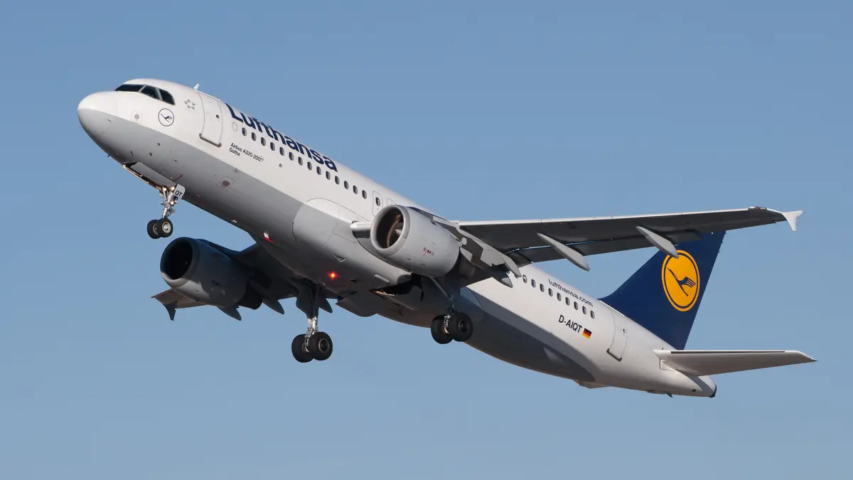 A Lufthansa Airbus A320 climbing steeply after take-off, landing gear still extended.