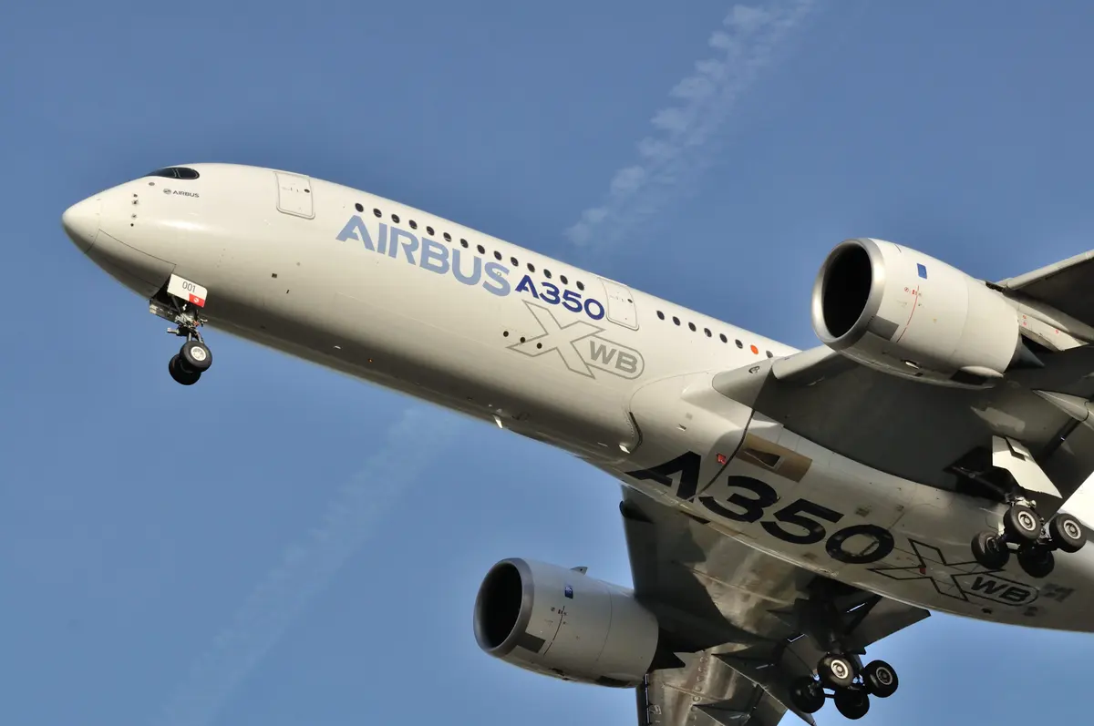 The nose and left engine of an Airbus A350 seen from below on approach, landing gear extended.