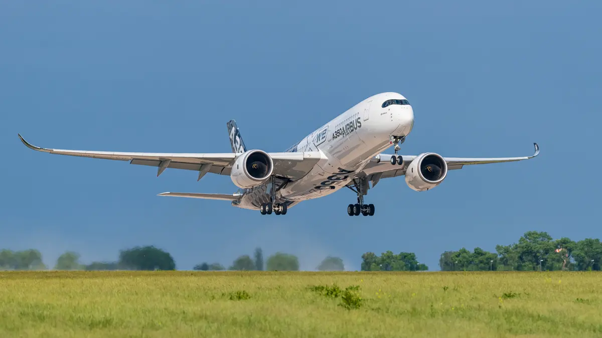 An Airbus A350 lifting off over a grass field under a deep blue sky, landing gear still extended.
