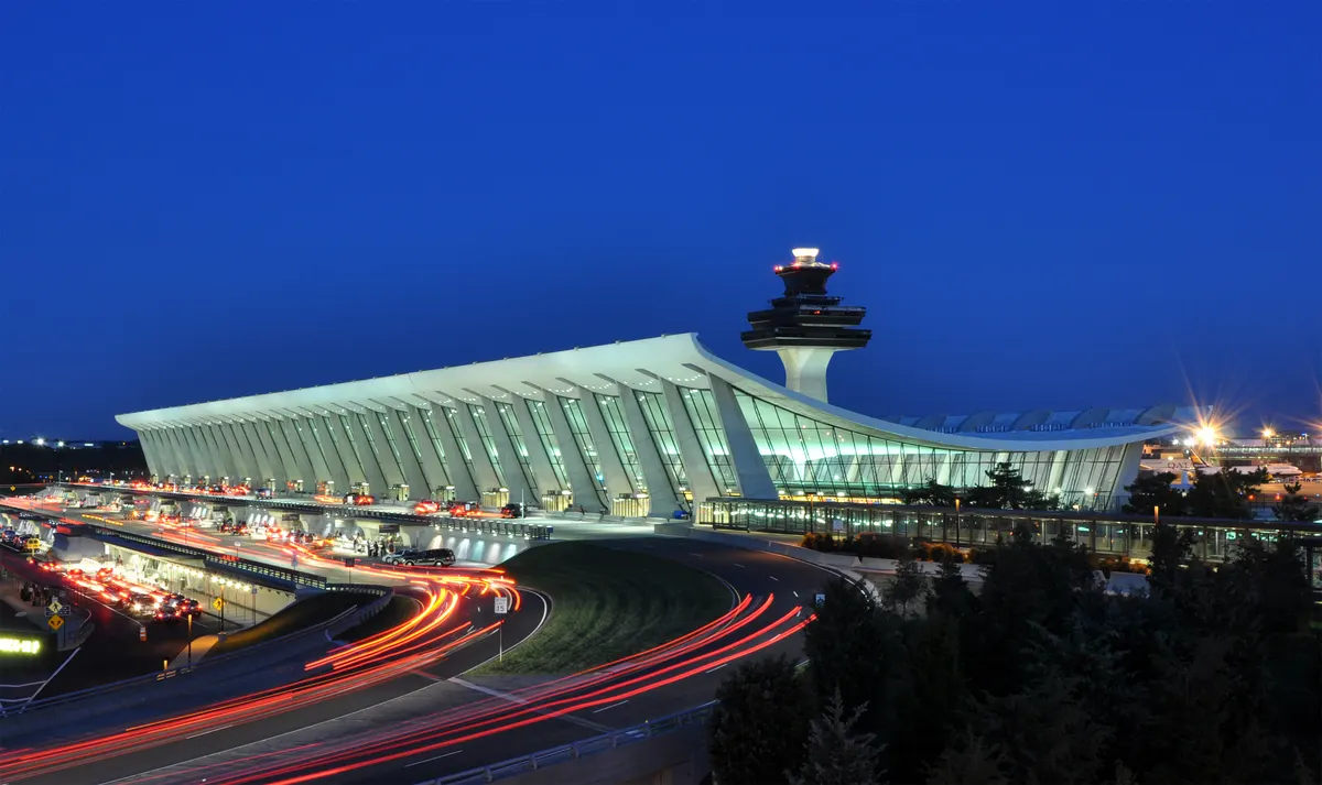 Washington Dulles International Airport at dusk, with the terminal and control tower lit and light trails from traffic in front.