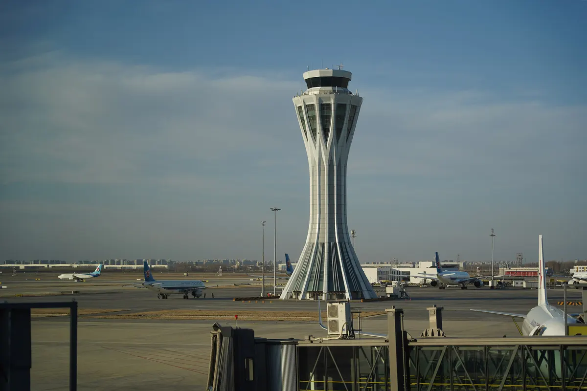 The control tower of Beijing Daxing International Airport rising above the apron, with airliners parked beside the terminal.