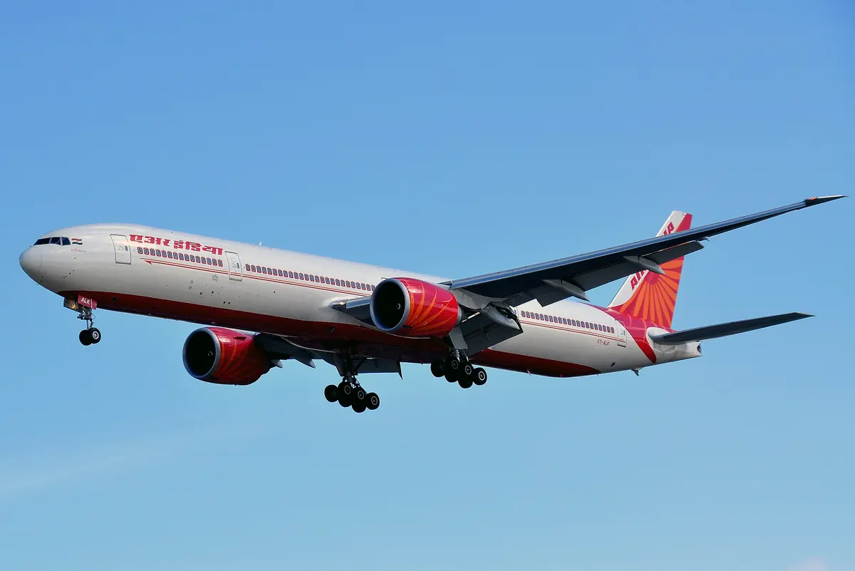 An Air India Boeing 777-300ER on approach against a bright blue sky, landing gear extended.