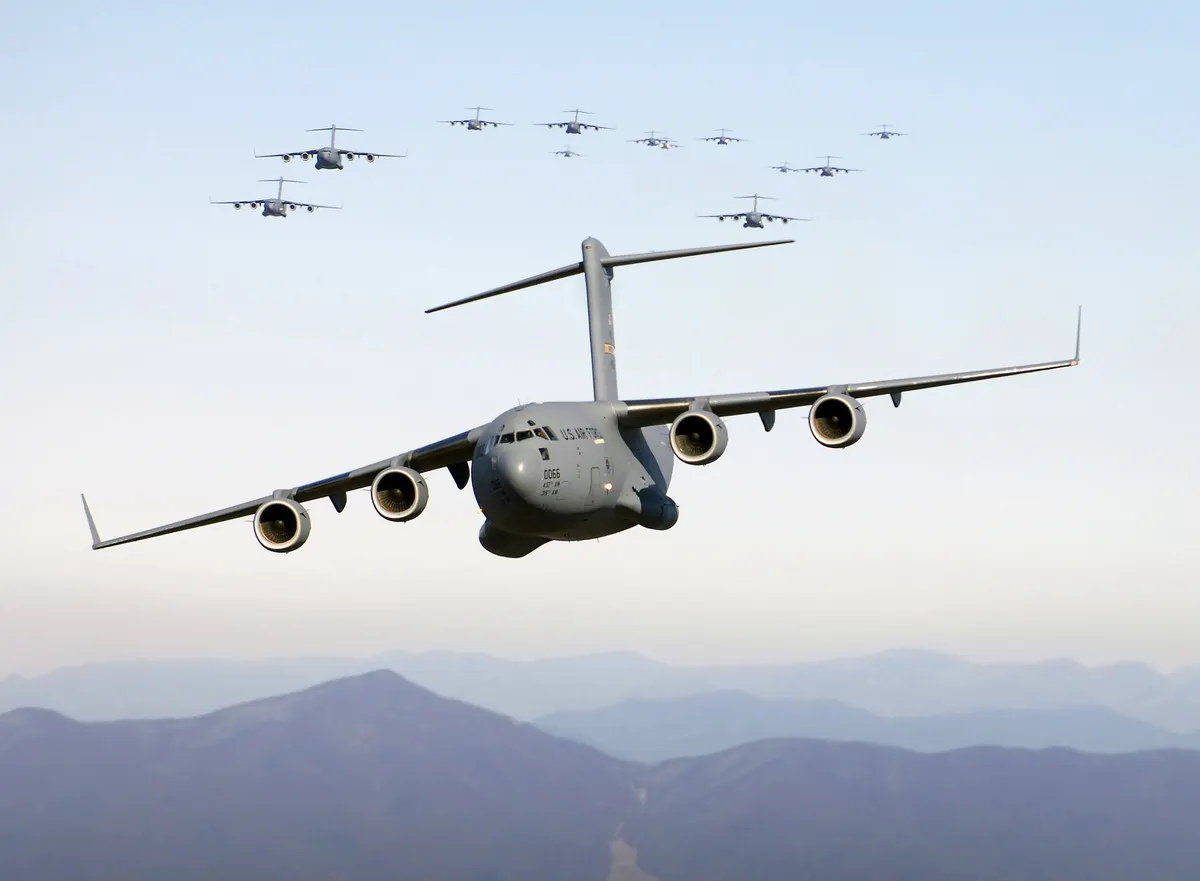 A C-17 Globemaster III in flight over the Blue Ridge Mountains, with a formation of other aircraft far behind it.