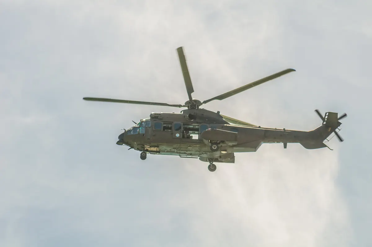 An Airbus Helicopters EC725 Super Cougar in military service flying over Recife Bay against an overcast sky.