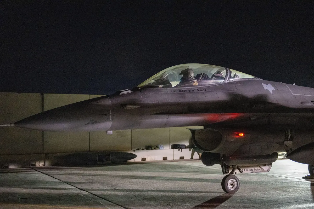 An F-16 Fighting Falcon on the ground at night with its canopy lit, preparing to take off.